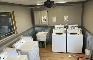 A laundry room with three white washing machines, a utility sink, a wall cabinet, and a ceiling fan. A laundry room with three white washing machines, a utility sink, a wall cabinet, and a ceiling fan.