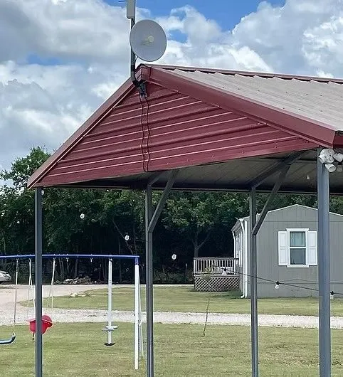 A small parabolic antenna mounted on the corner of a metal-roofed structure next to a yard with a swing set. A small parabolic antenna mounted on the corner of a metal-roofed structure next to a yard with a swing set.